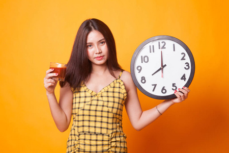 年轻的亚洲妇女与蕃茄汁液和时钟在黄色背景