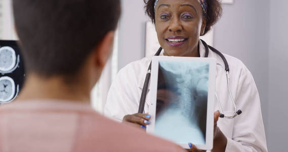迷人的资深黑人医生指着 x 线患者颈部疼痛的来源