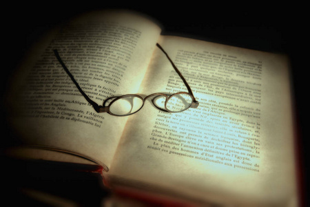 特写镜头非常老眼镜眼睛眼镜上非常老的闭合的书躺在镜子在光束之下。复古仍然生活, 在黑暗的黑色背景。复制空间。黄金过滤器美丽的图片