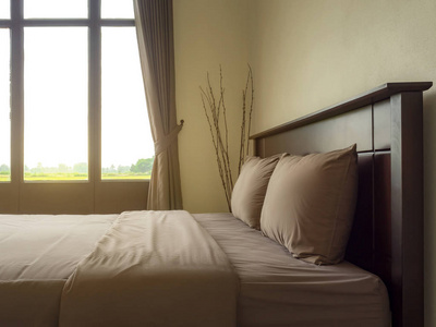 空的双人床在大窗户的一侧, 早晨的阳光在豪华和自然风格的卧室是简单的装饰与两个枕头