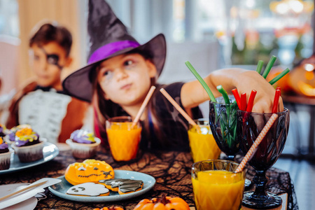 女孩戴巫师帽万圣节喝果汁和吃软糖糖果