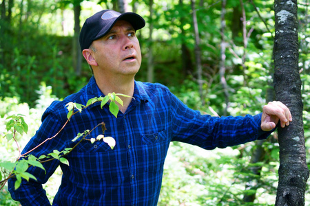 一位好奇的白种人在森林里散步时, 穿着一件蓝色格子衬衫, 戴着一顶黑色的帽子, 把目光移开