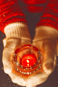 举行圣诞蜡烛在温暖的手套的妇女