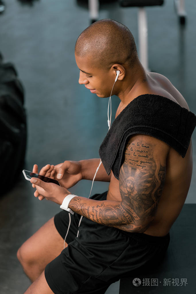 和使用智能手机在健身房的肌肉赤裸上身的非洲裔美国男子的高角度视图