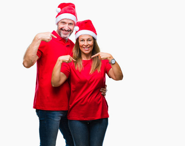 中年拉美裔夫妇穿着圣诞节帽子在孤立的背景看自信与微笑在脸上, 指着自己与手指自豪和快乐