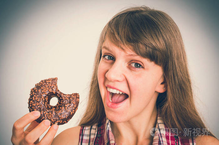 迷人的女人正在吃一个美味的甜甜圈灰色背景-复古风格