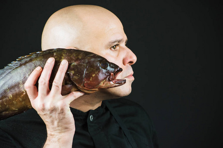 厨师在黑色背景上持有大鱼在张开的嘴巴贴近他的脸的特写镜头