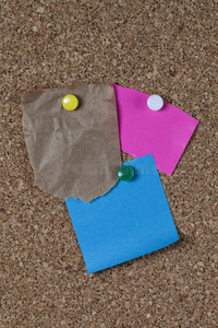 在软木板上撕碎的棕色纸袋，上面有彩色的纸条和别针。