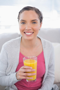 微笑的女人坐在沙发上拿着橙汁