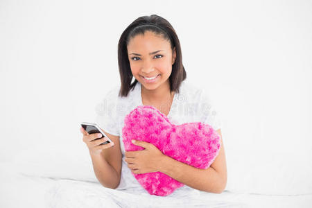 开心的黑发年轻模特抱着枕头和手机