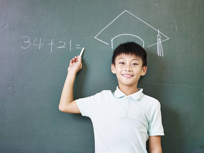 站在粉笔绘制的博士帽下的亚洲小学男生照片