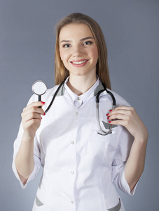 穿白色制服的女医生认为听诊器和微笑。模糊的人影
