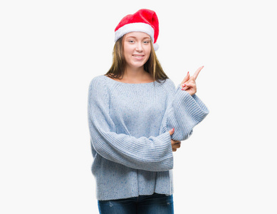 年轻美丽的白人妇女戴着圣诞节帽子在孤立的背景与一个大微笑在脸上, 指着手和手指在一边看着相机
