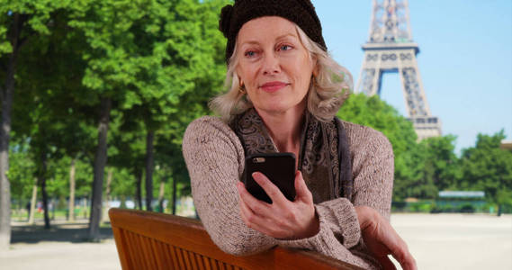 巴黎的老年女游客用手机在埃菲尔铁塔前发短信