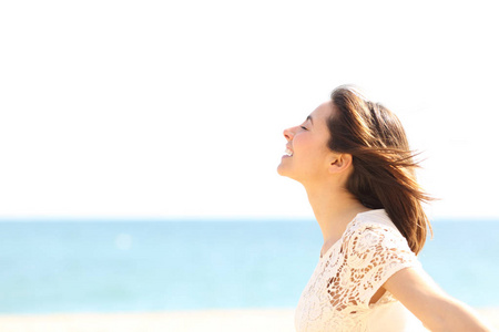 一个笑容满面的女士呼吸着深新鲜空气, 在海滩上享受风的侧视图肖像