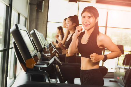 在现代体育健身房里, 有一群年轻人在跑步机上跑步或慢跑的快乐女人。运动和运动概念