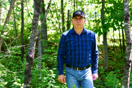 一名白种人穿着蓝色格子衬衫和黑色帽子在森林里徒步时看着我们