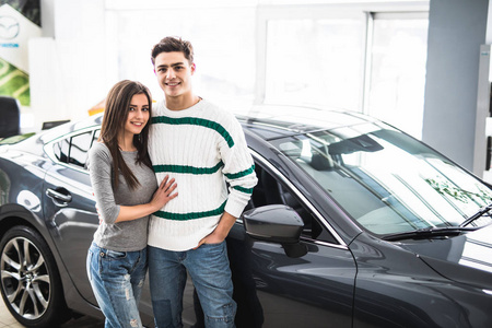 美丽的年轻夫妇站在汽车经销店和使他们的决定