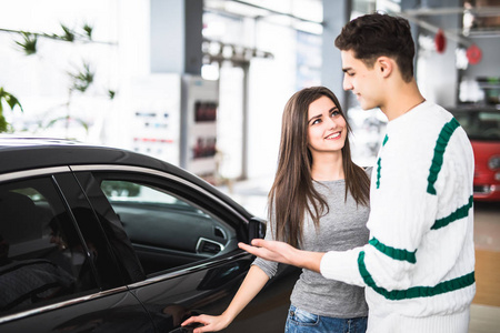 美丽的年轻夫妇站在经销商选择买一部车