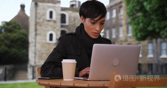 伦敦的非裔美国女性坐在外面的时候, 在笔记本电脑上愉快地打字