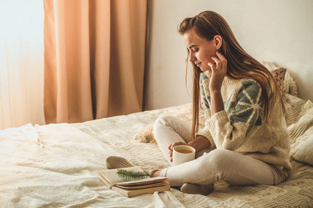 舒适的家。美丽的女孩正在床上看书。早上好, 喝茶。漂亮的年轻女孩放松。阅读的概念