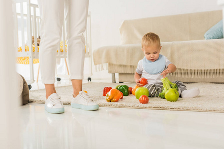 裁剪腿站在幼儿旁边坐在地板上玩水果和蔬菜