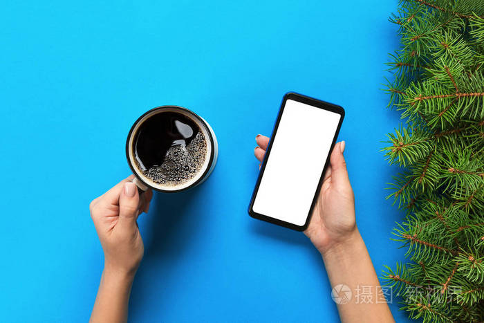 女性手持黑色手机与空白的白色屏幕和杯咖啡。具有复制空间的模型图像。在蓝色背景上的顶部视图, 平躺
