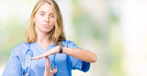美丽的年轻医生妇女穿着医疗制服在孤立的背景做时间用手的手势, 沮丧和严肃的脸