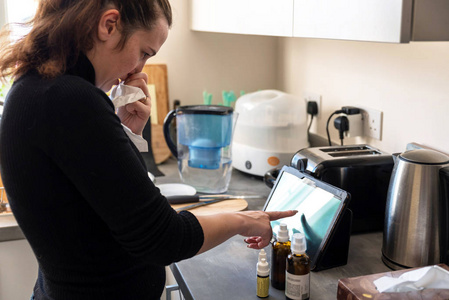 年轻的生病的妇女工作从家庭厨房在片剂旁边的药物照片