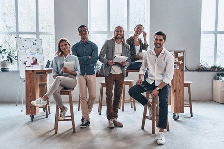 一群快乐微笑的人在木桌上在创造性的现代办公室工作室摆姿势和看着相机