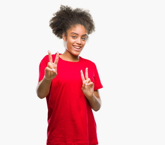 年轻的美国黑人妇女在孤立的背景下微笑着看着相机显示手指做胜利标志。第二个