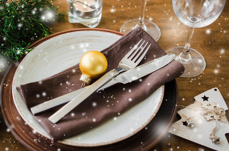 简单的圣诞餐桌的地方设置在木制背景的复古或乡村风格。节日餐桌设置为圣诞节或新年晚餐。雪效果