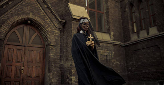 寺外纸祈祷美丽的年轻修女在黑色的马甲, 斗篷和透明的斗篷站在和祈祷