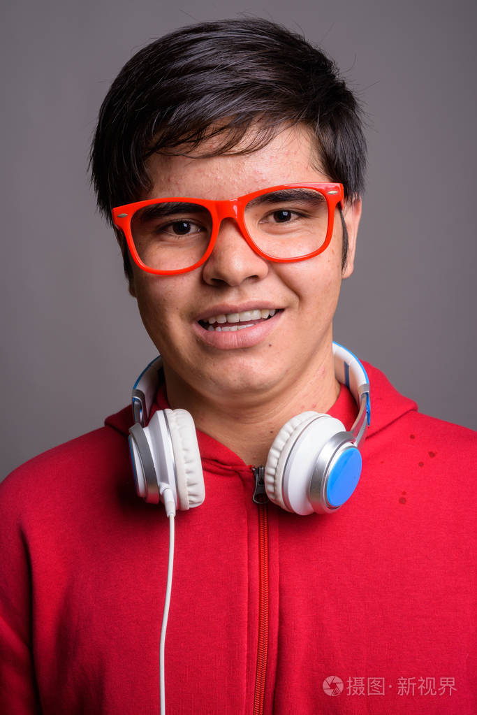 年轻的亚洲十几岁的男孩戴着耳机反对灰色的背景