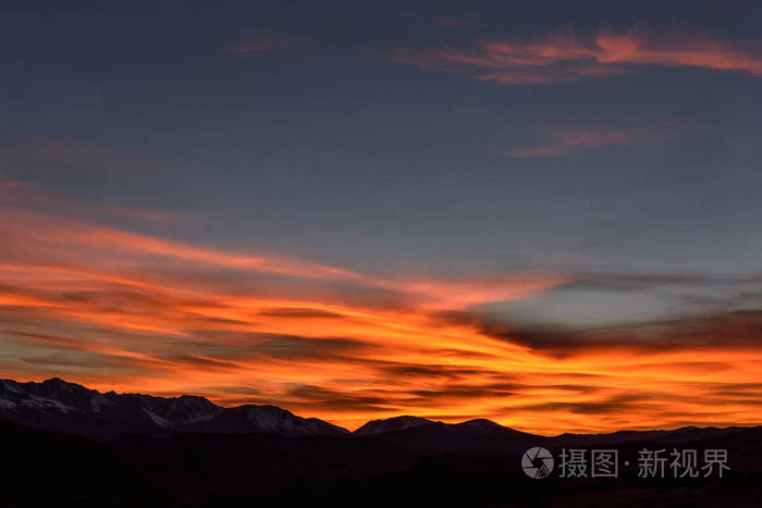 在日落时被雪覆盖的山上的蓝天上, 粉红色和火热的卷云令人惊叹