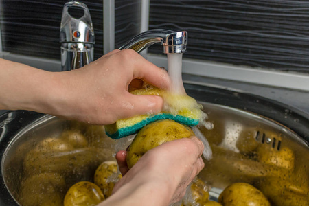在自来水下清洗蔬菜。人的手洗生土豆