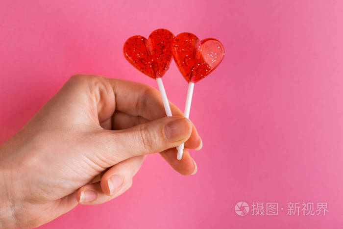 两个甜美明亮的红色棒棒糖在女人的手在明亮的粉红色背景.复制空间