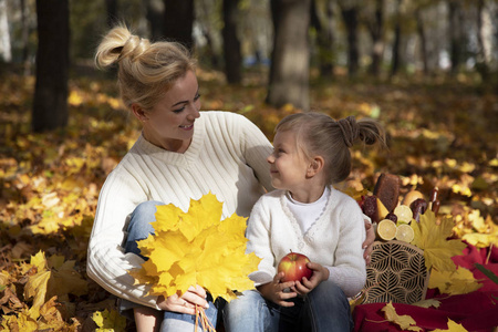 妈妈和女儿在公园里。秋天和黄色的叶子。年轻的母亲和她的幼儿女孩有乐趣