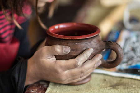年轻的女孩肮脏的粘土手里拿着一个陶瓷杯，她自制陶器学校在陶工车轮。选择性的焦点