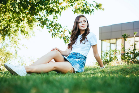 美丽的女孩坐在绿色的草地上公园, 看着远离