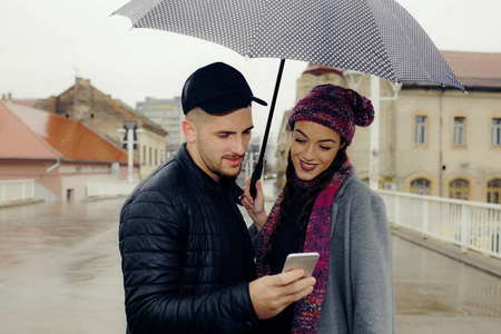 愉快的夫妇, 年轻人和一个妇女用一把雨伞在城市使用手机