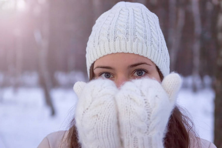 一个戴着白色针织手套和帽子的女孩。背景中的雪林。冬天。雪在附近