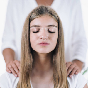 和平的女孩坐在她的眼睛闭着, 接受灵气治疗的女性灵气治疗。灵气医生站在美丽的青少年患者的肩膀上按摩。替代疗法概念