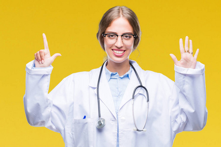 美丽的年轻金发碧眼的医生妇女穿着医疗制服在孤立的背景显示和手指指向数字 7, 而微笑着自信和快乐