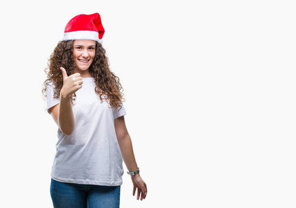 年轻的黑发女孩戴着圣诞帽在孤立的背景做快乐的大拇指与手的手势。通过显示成功来批准镜头的表达