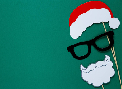 照相馆五颜六色的道具为圣诞晚会圣诞老人帽子, 眼镜, 胡子在绿色背景。圣诞节和新年装饰品