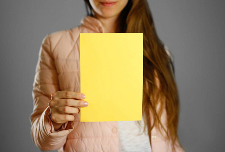 穿着温暖的冬衣的女人拿着黄色的传单。空白纸张。闭上你的嘴隔离的背景