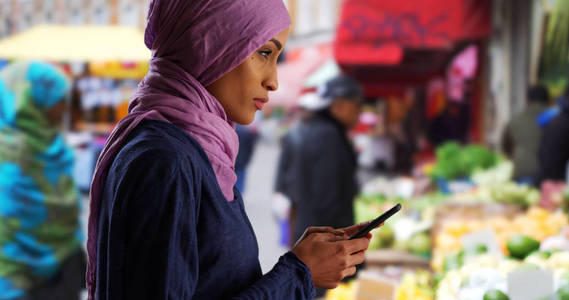 美丽的年轻穆斯林妇女用智能手机发短信外