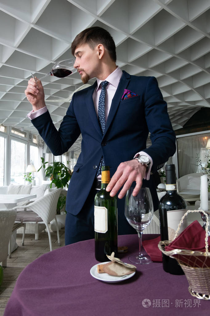 年轻的男性侍酒师倒在一个饮水机, 而品尝红酒