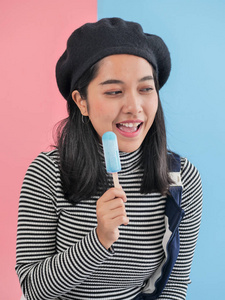 愉快的亚洲妇女吃蓝色冰淇淋棍子与颜色背景